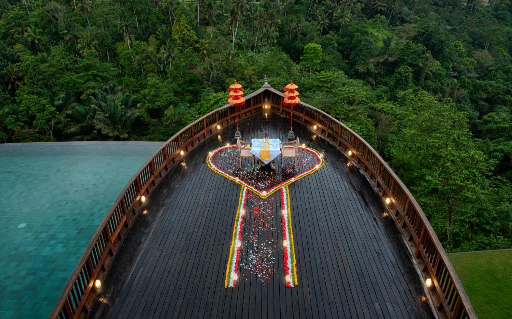 Romantic dining setup on a wooden deck shaped like a boat, adorned with flower petals in a heart design, overlooking lush jungle—an enchanting experience at wellness retreats in Bali.
