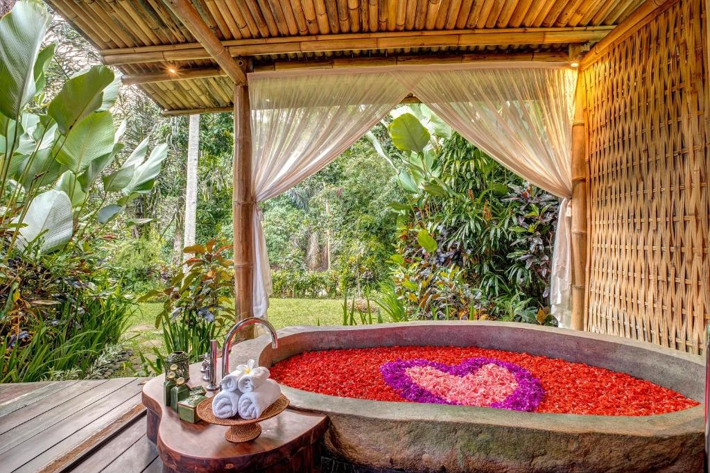 Open-air stone bathtub filled with red and pink flower petals in a heart shape, surrounded by lush tropical greenery at a luxury spa—perfect for wellness retreats in Bali.