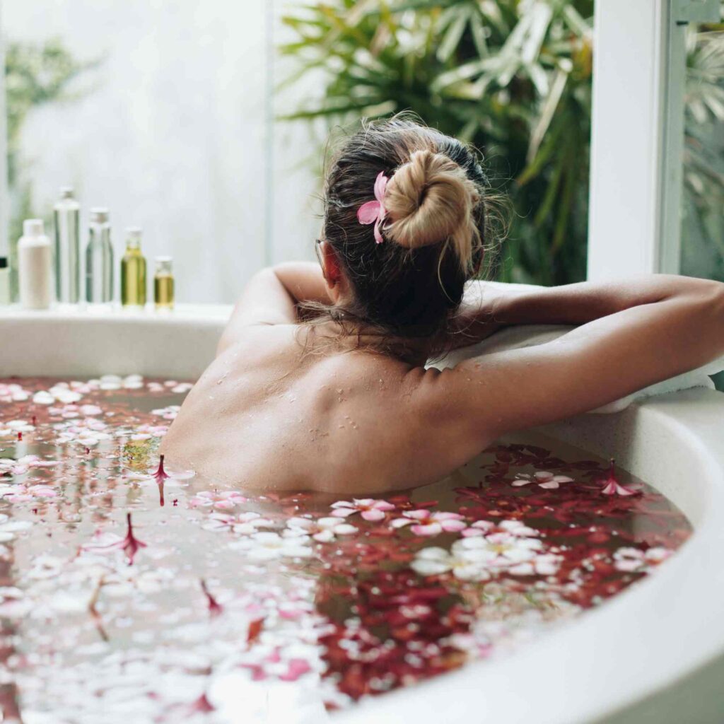  Pink petals fill a bath with a women relaxing and enjoying the best flower bath in Bali