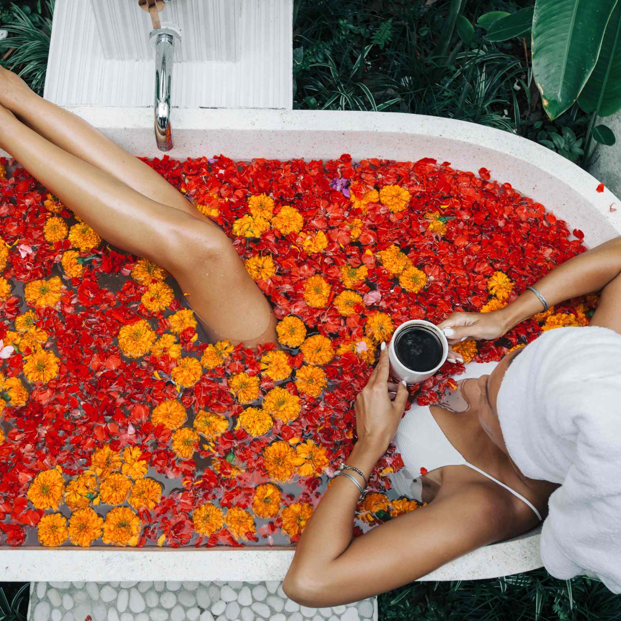 Red and orange petals fill a bath with a women relaxing and enjoying the best flower bath in Bali