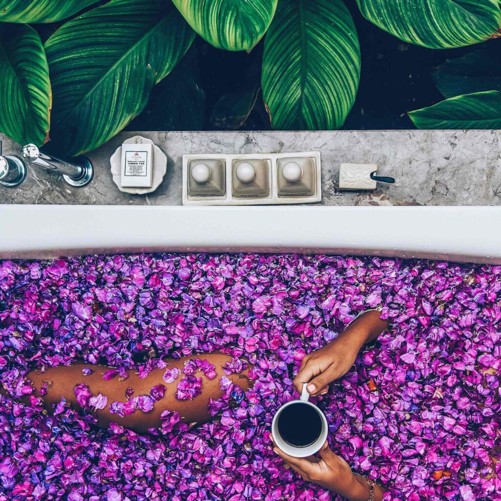 Purple petals fill a bath with a women relaxing and enjoying the best flower bath in Bali