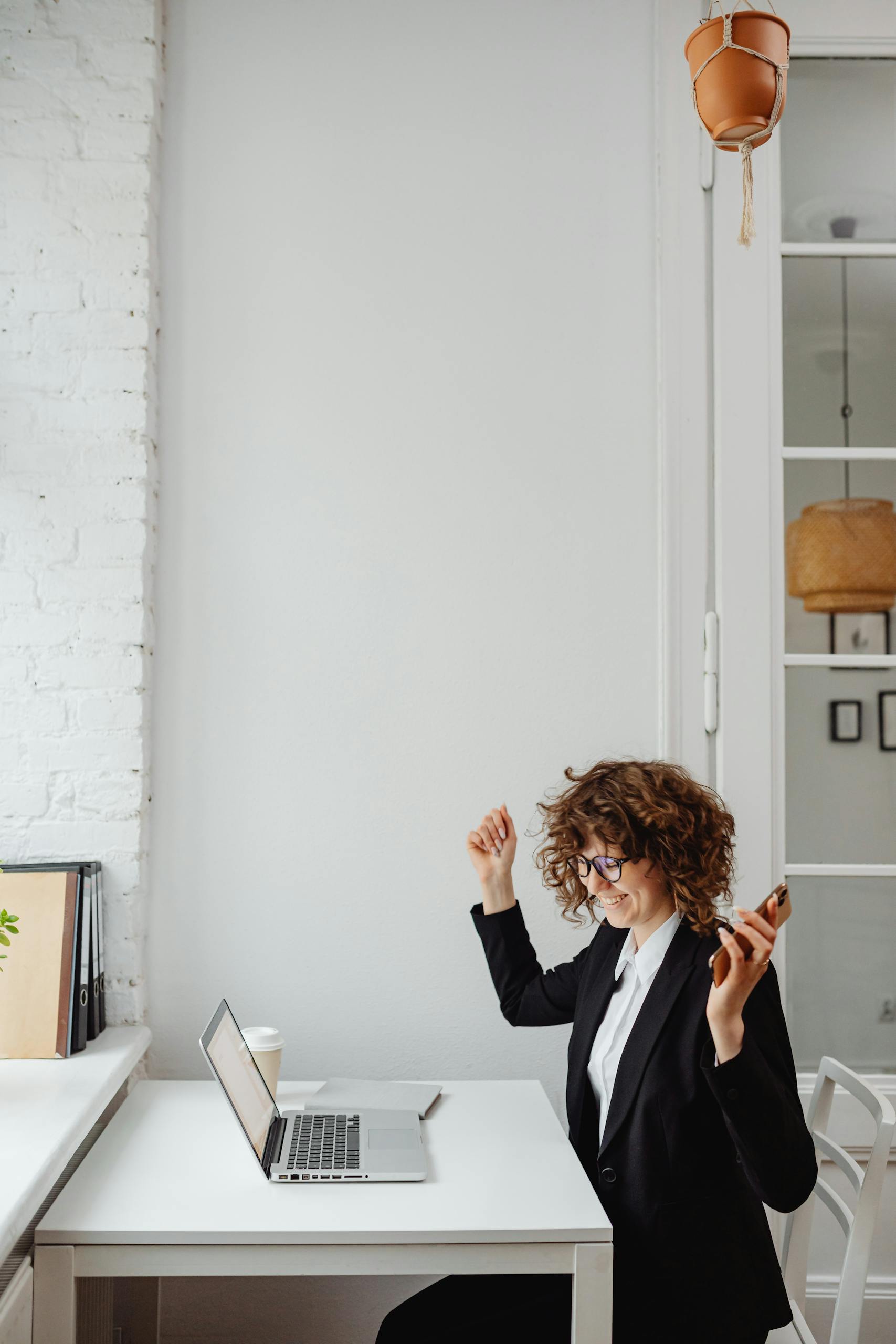 A female lawyer in Black Blazer Sitting in Front of the Table with Laptop with her hands up rejoicing because she achieved financial independence
