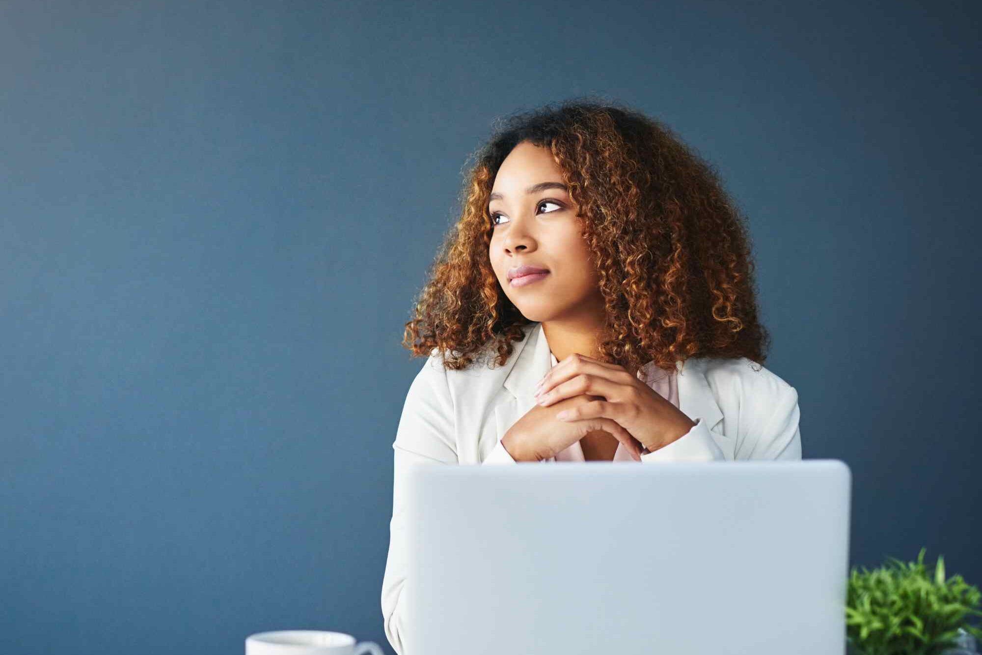 Black woman in business attire looking away from her laptop