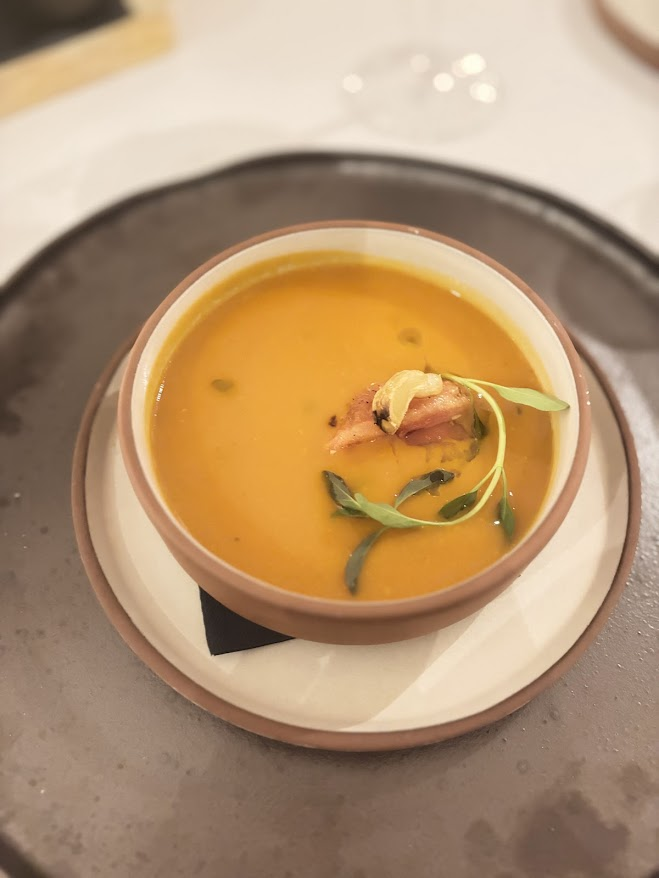 Elegant orange soup with garnish served in ceramic bowl on dark plate at fine dining restaurant