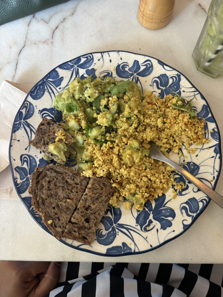 Scrambled tofu with avocado and herbs served with dark bread on blue floral plate - healthy vegan breakfast meal
