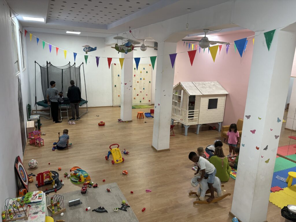 Indoor children's playroom with trampoline, playhouse, climbing wall, toys and colorful triangle banner decorations