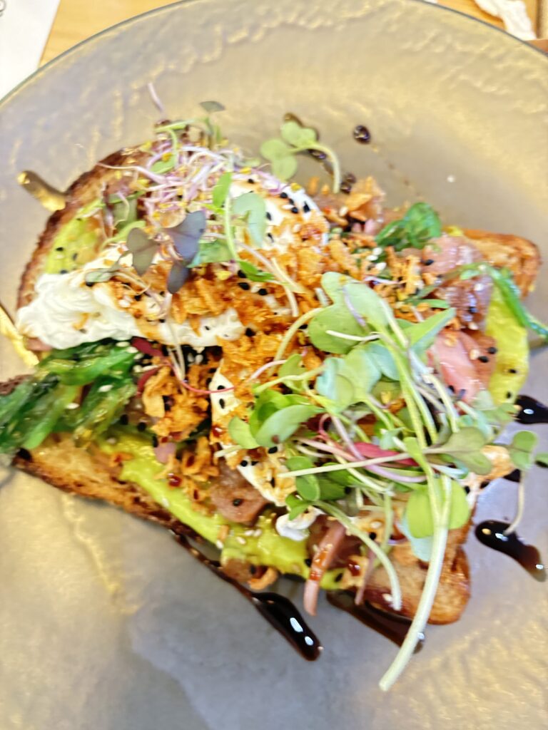 Gourmet avocado toast topped with microgreens, sprouts, and balsamic drizzle served on clear glass plate