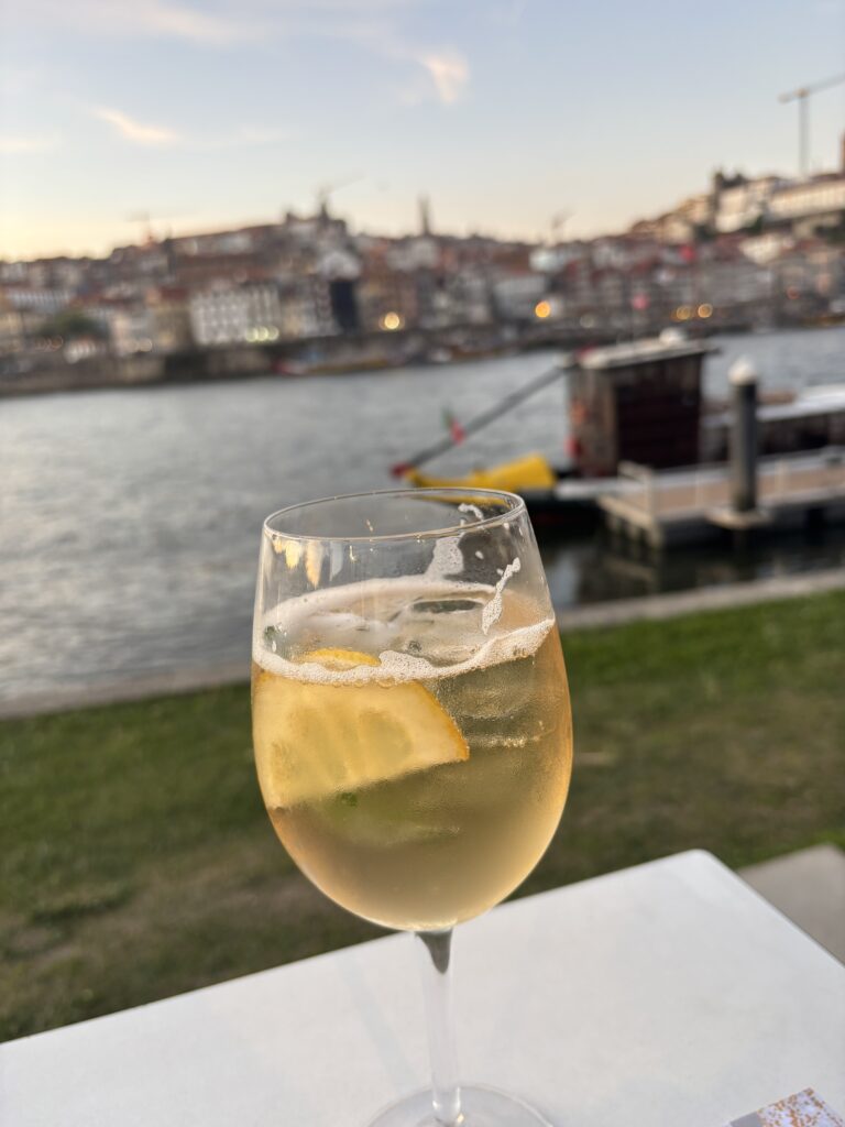 Glass of white wine with lemon slice overlooking Porto riverside at sunset with boats and historic buildings