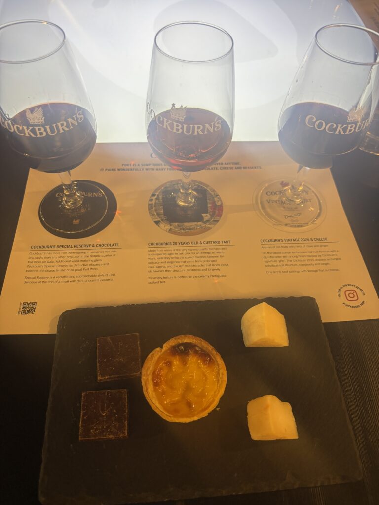 Cockburn's Port wine tasting with three glasses and paired chocolates, custard tart, and cheese on slate board