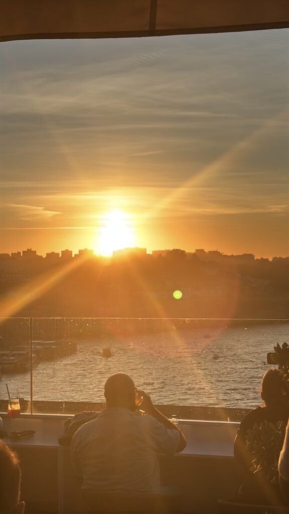 Sunset view over waterfront city skyline with people dining at restaurant terrace overlooking harbor and buildings