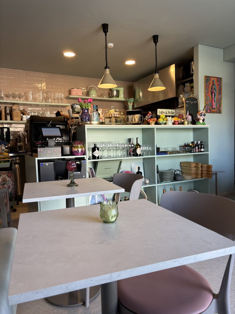 Modern cafe interior with white tables, pendant lights, open shelving with glassware, and espresso machine