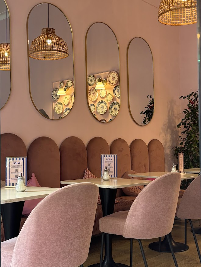 Modern restaurant interior with pink upholstered chairs, oval mirrors, wicker pendant lights, and arched banquette seating