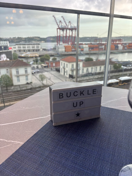 Lightbox with 'BUCKLE UP' message on desk overlooking port city with cargo cranes and waterfront view