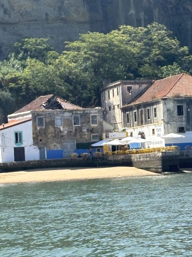 Coastal village with historic stone buildings, beach, and lush green cliffs overlooking turquoise water