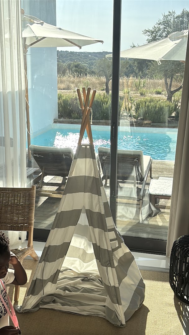 Luxury poolside teepee tent with striped awning, lounge chairs, and countryside views in Mediterranean resort setting.