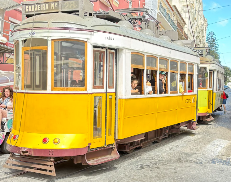 Yellow vintage tram number 28 on Lisbon street with passengers and historic buildings.